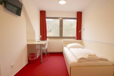 Komfortables Einzelzimmer mit eigenem Fernseher und Schreibtisch